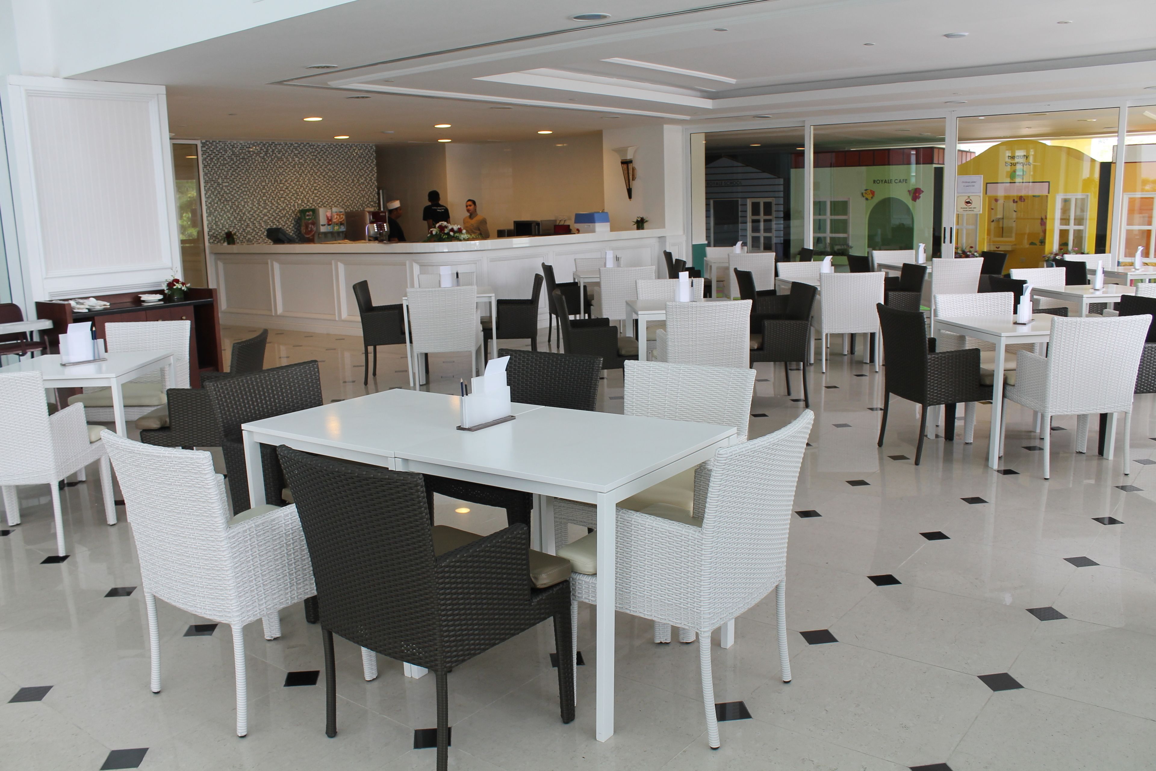 A modern restaurant with white tables and chairs, a bar area, and a visible kitchen.