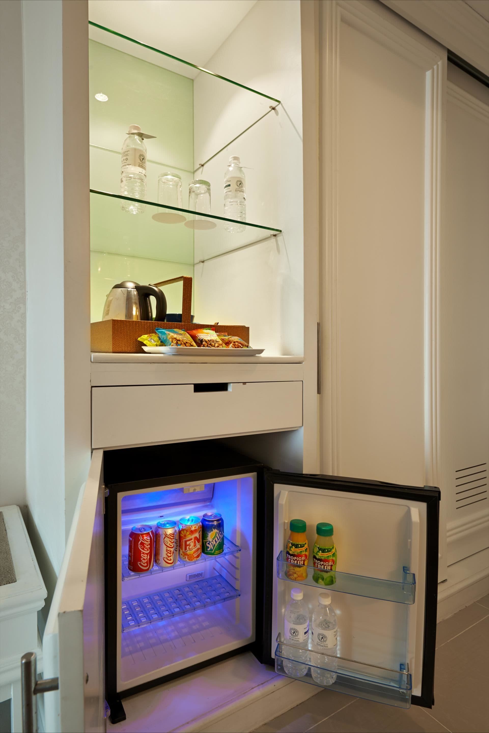A compact refrigerator with a glass shelf above and a freezer below, containing beverages and snacks.