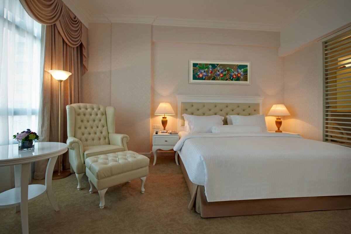 A hotel room with a large bed, a chair, a table, and a nightstand with lamps.