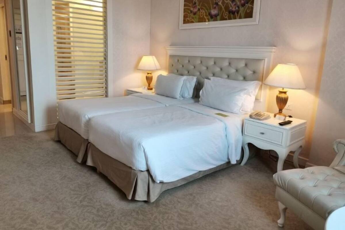 A neatly arranged hotel room with a large bed, two bedside tables with lamps, a chair, and a painting on the wall.