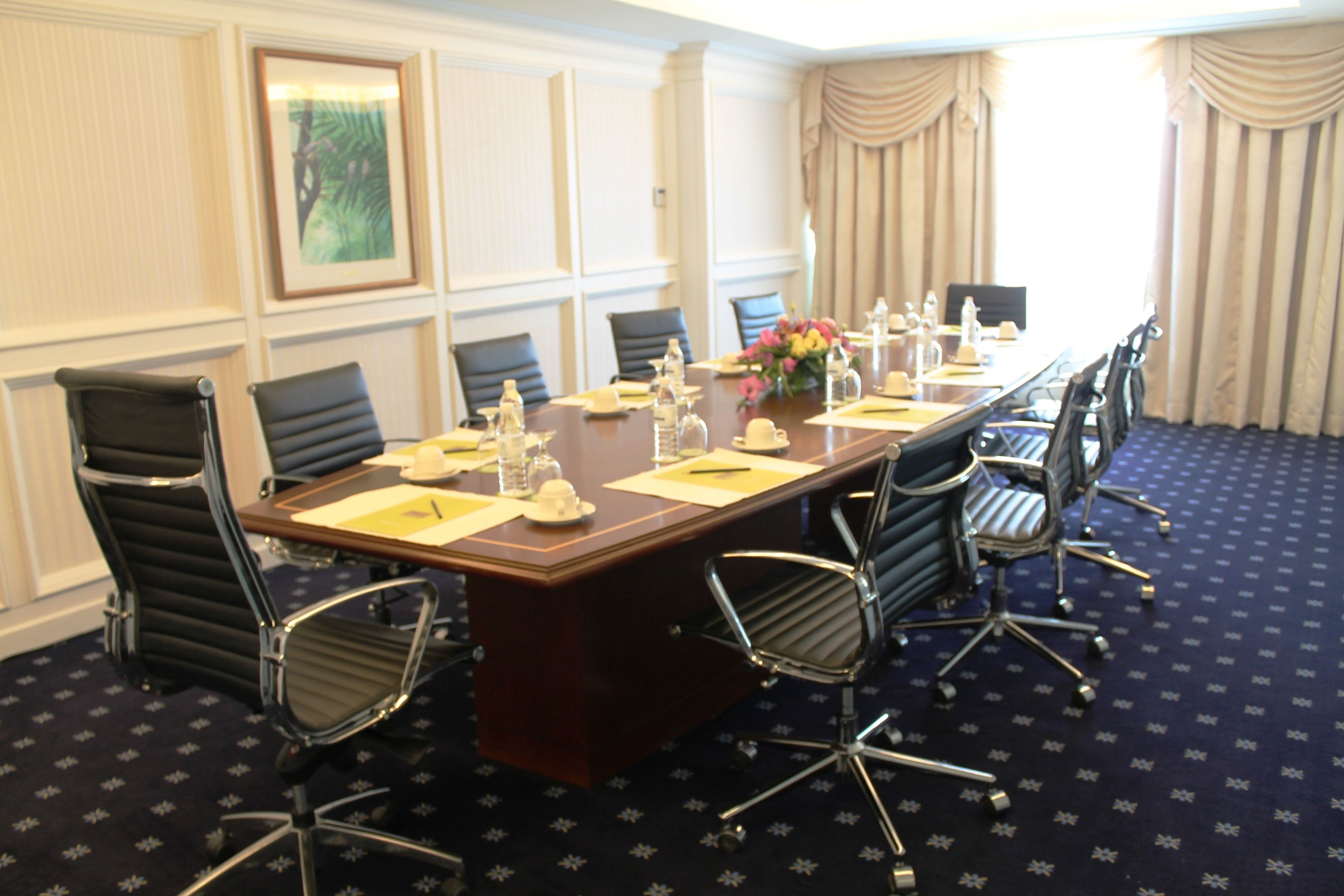Une salle de conférence avec une longue table, des chaises et un arrangement floral au centre.