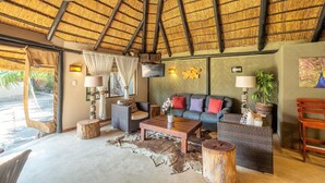 A room with a thatched roof, wicker furniture, a wooden coffee table, and a view of the outdoors. - Gecko Ridge Guest House (Swakopmund)