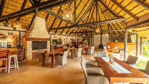 A spacious indoor area with a high thatched roof, stone fireplace, and wooden furniture. - Gecko Ridge Guest House (Swakopmund)