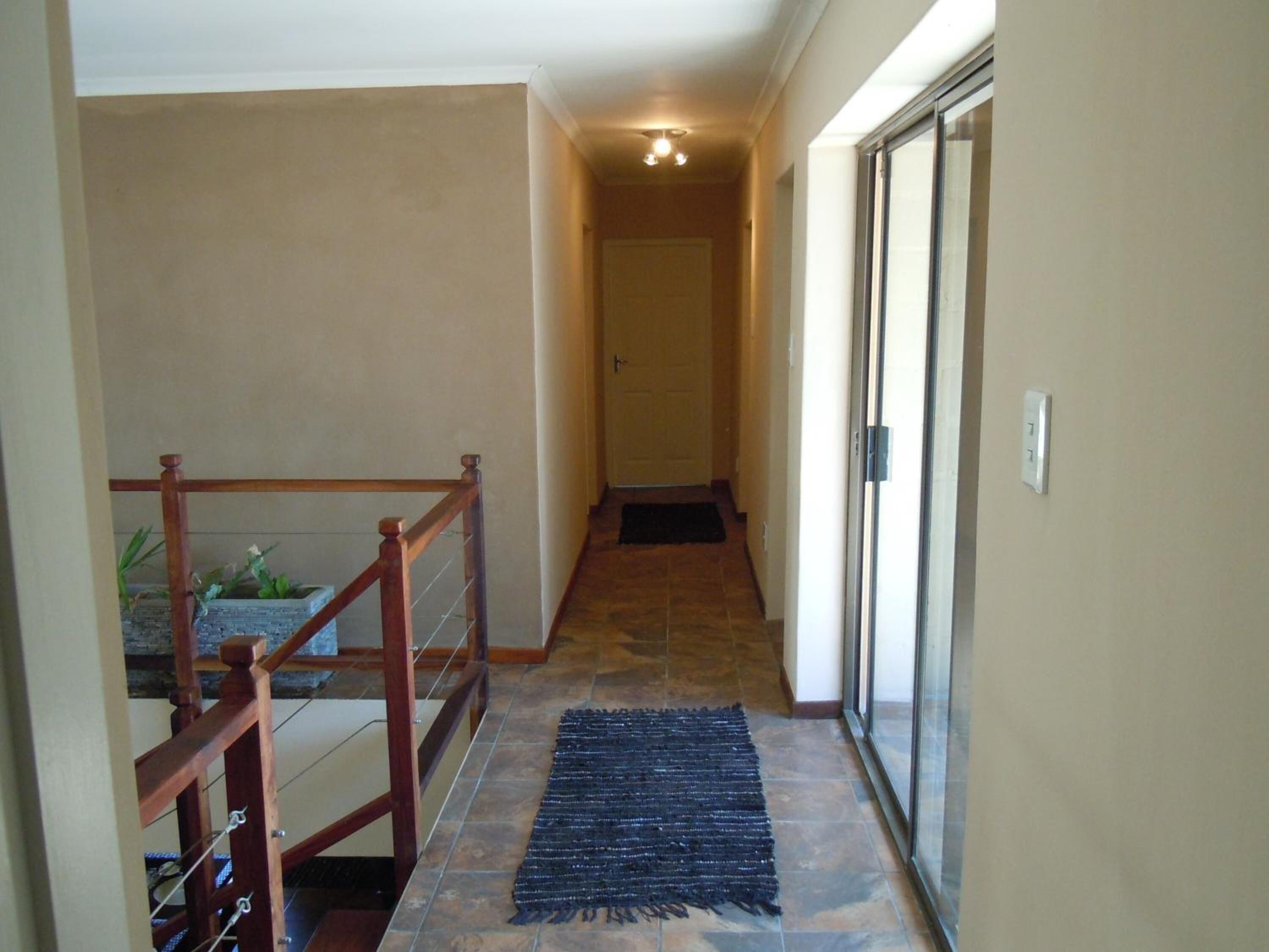 A hallway with a wooden railing, a black rug, and a glass door leading to another room.