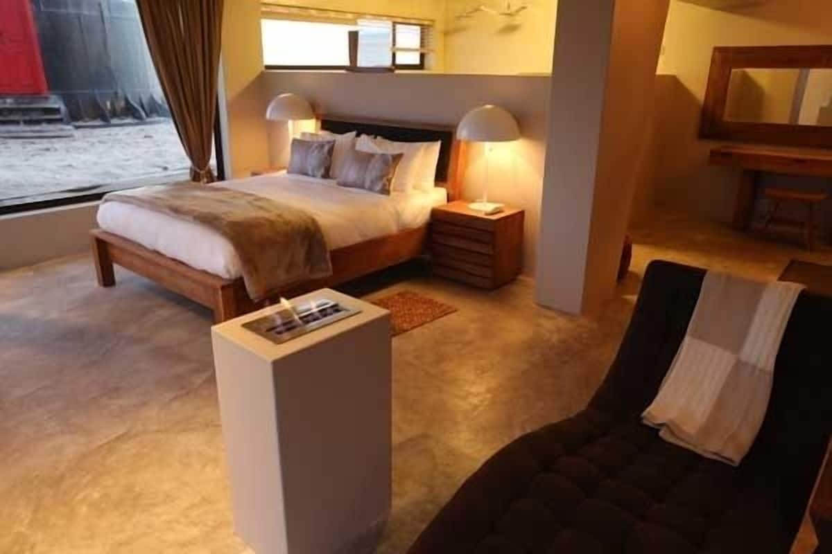 A bedroom with a bed, bedside lamps, a nightstand, a chair, and a small table with a magazine.