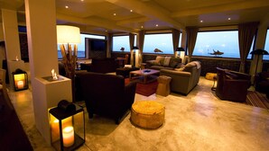 A spacious living area with comfortable seating, a large window offering a view of the sea, and a fireplace. - Pelican Point Lodge (Walvis Bay)