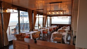 A restaurant with wooden furniture, white tablecloths, and hanging lights. - Pelican Point Lodge (Walvis Bay)