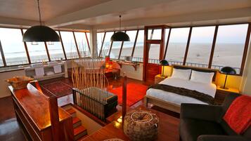 Une chambre moderne avec un lit, un canapé, une table en bois et une grande fenêtre donnant sur l’océan.