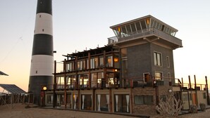A multi-story building with a prominent lighthouse structure adjacent to it. - Pelican Point Lodge (Walvis Bay)