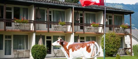 A building with a balcony, a Swiss flag, and a cow statue in the yard.