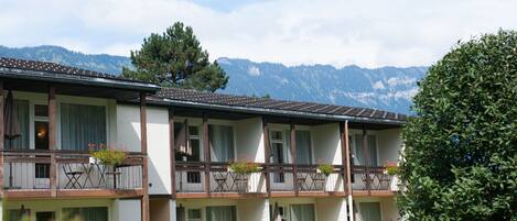 A multi-story hotel with balconies, each with a small table and chairs, and potted plants.