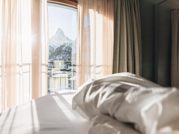 Habitación de hotel con cama, cortinas y ventana con vista a la montaña.