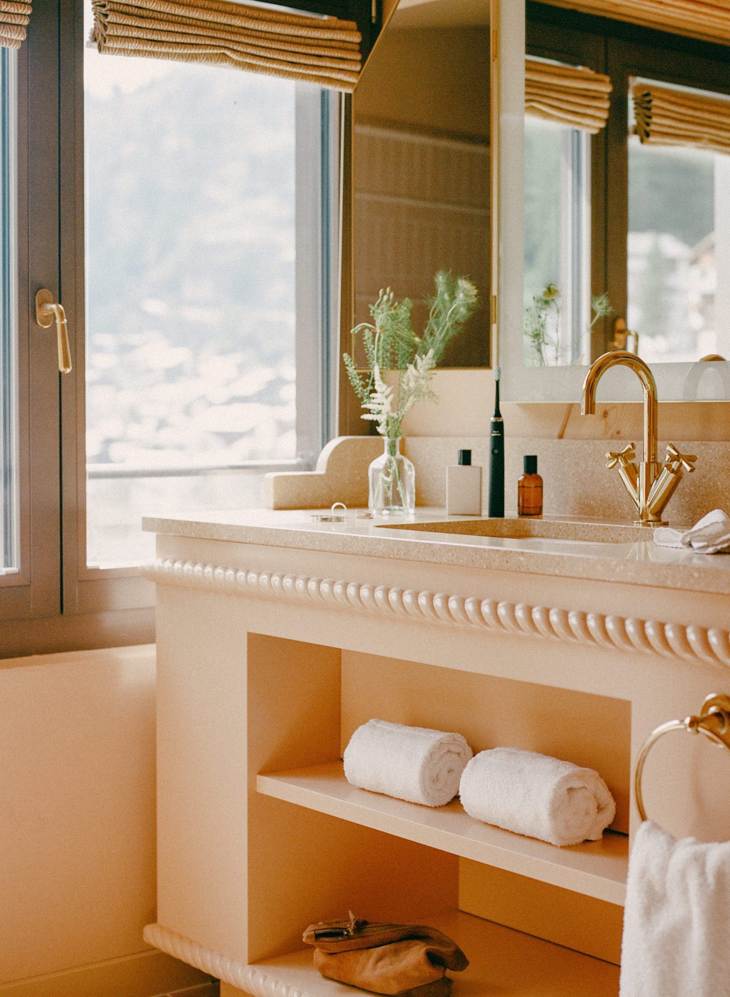 Une salle de bain avec un meuble-lavabo beige, un robinet doré et un miroir au-dessus du lavabo.