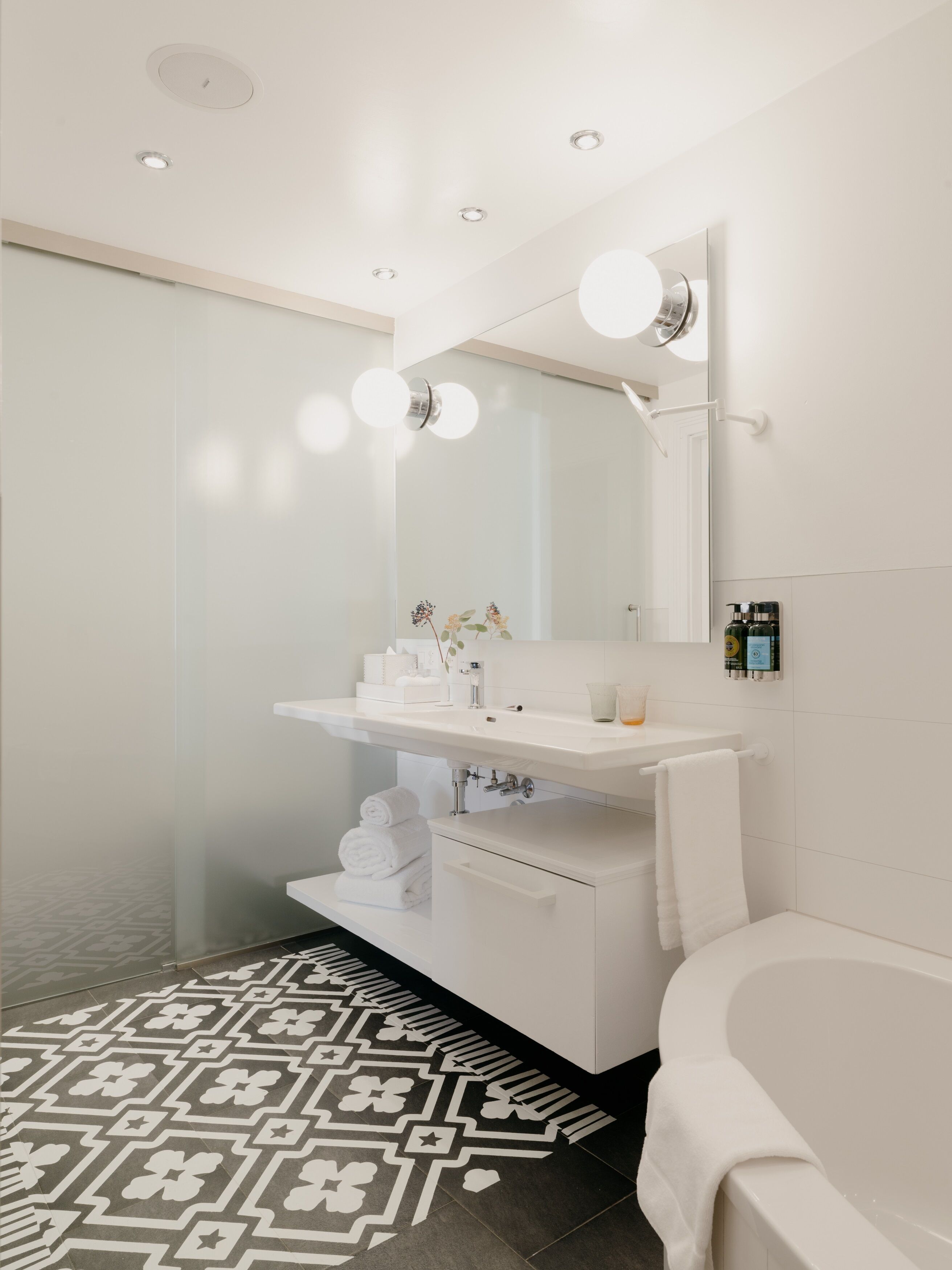 A modern bathroom with a white sink, mirror, and bathtub. There are towels and toiletries on the counter.