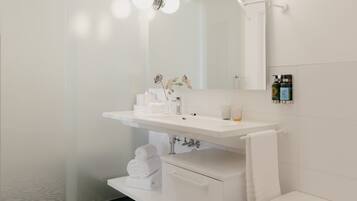 A modern bathroom with a white sink, mirror, and bathtub. There are towels and toiletries on the counter.