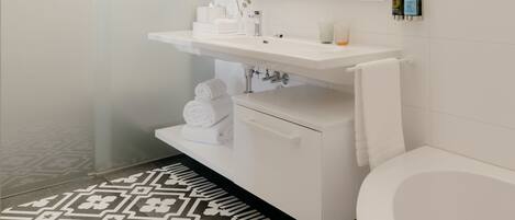 A modern bathroom with a white sink, mirror, and bathtub. There are towels and toiletries on the counter.
