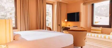 A hotel room with a large bed, a desk, a chair, a TV, and a view of the mountains.