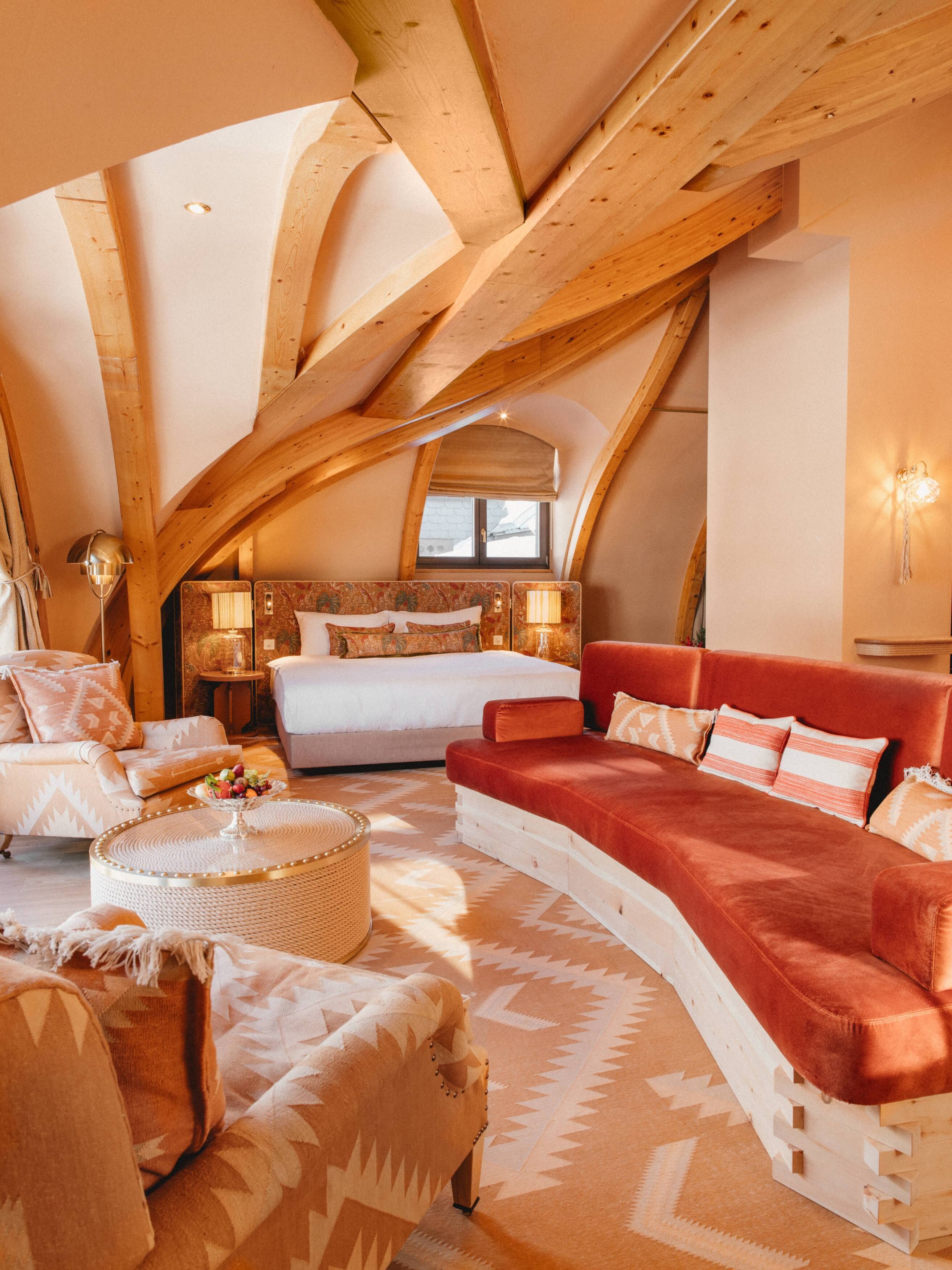 A cozy, well-lit attic bedroom with a large bed, a red sofa, and a patterned rug.