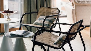 Ein modernes Wohnzimmer mit einem Korbstuhl, einem kleinen runden Tisch und Blick auf die Stadt durch große Fenster.