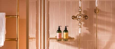 Een badkamer met een goudkleurig douchesysteem, een handdoekhouder en twee flessen op een plank.