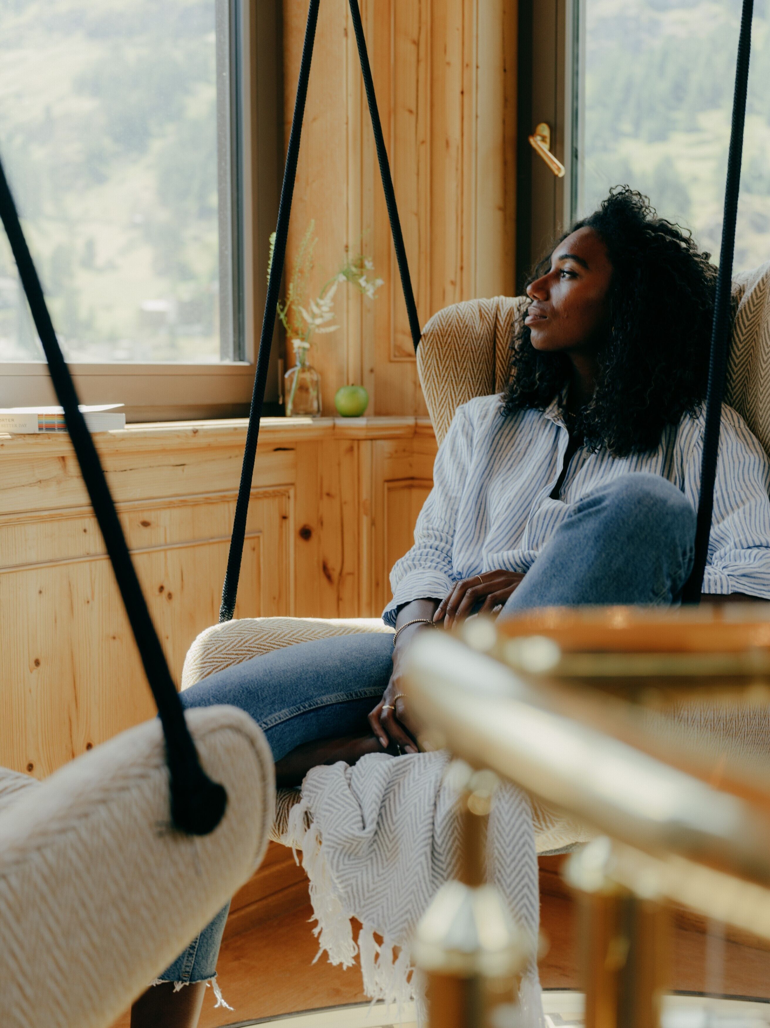 A person sitting on a swing chair in a room with wooden walls and a window.