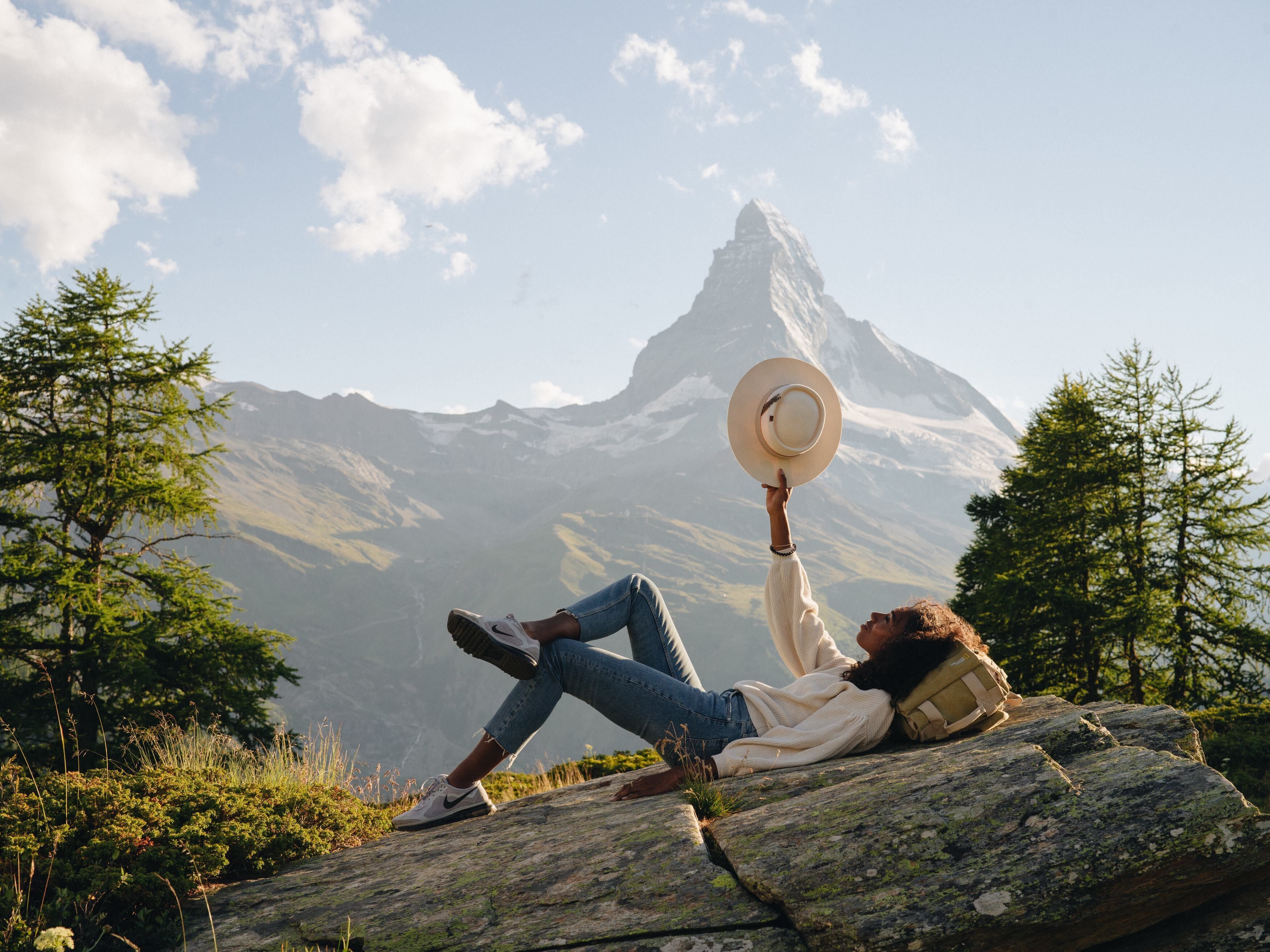 Une personne assise sur un rocher, avec une montagne en arrière-plan.