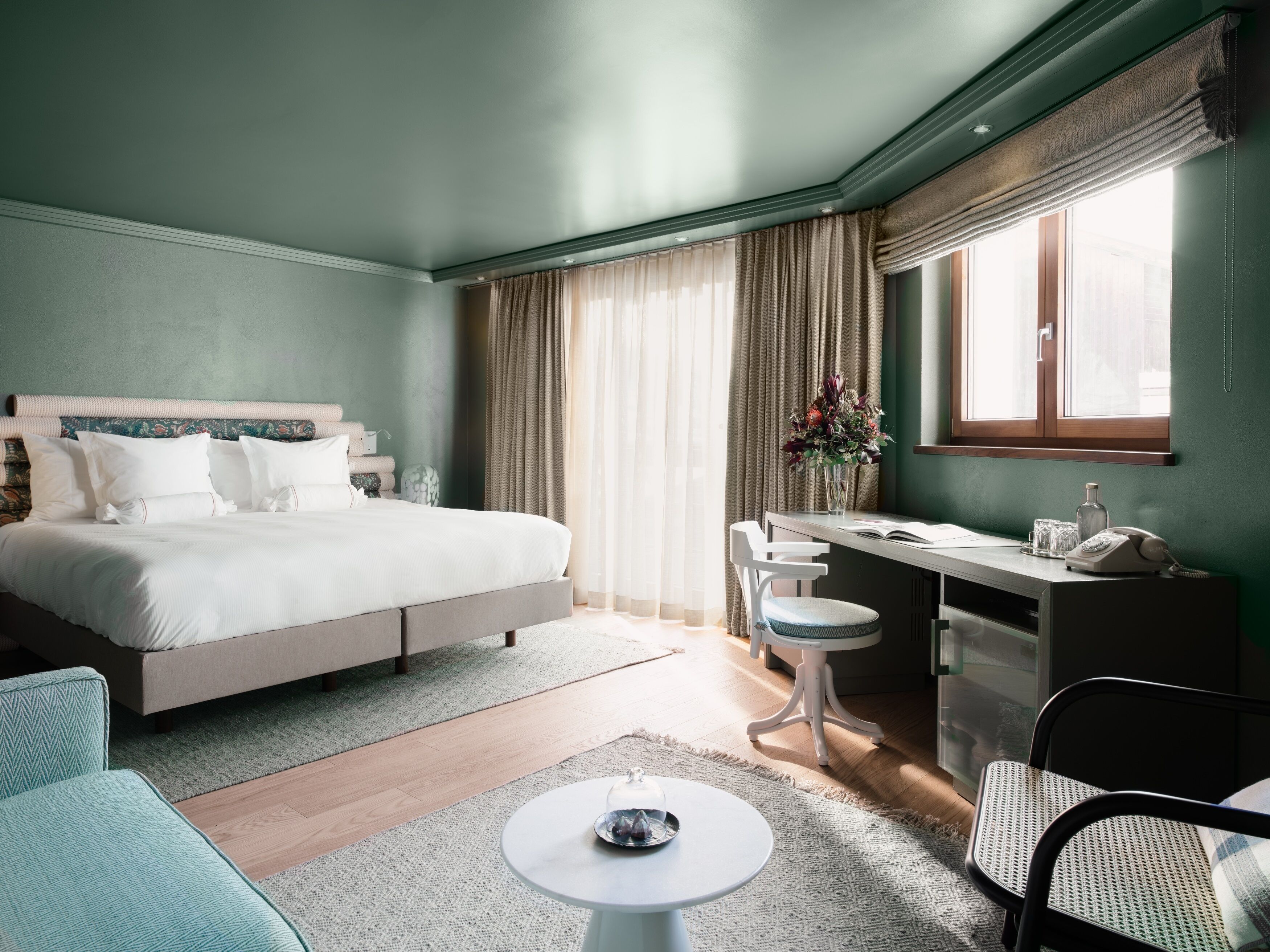 A hotel room with a bed, desk, chair, and a small table with a decorative item.
