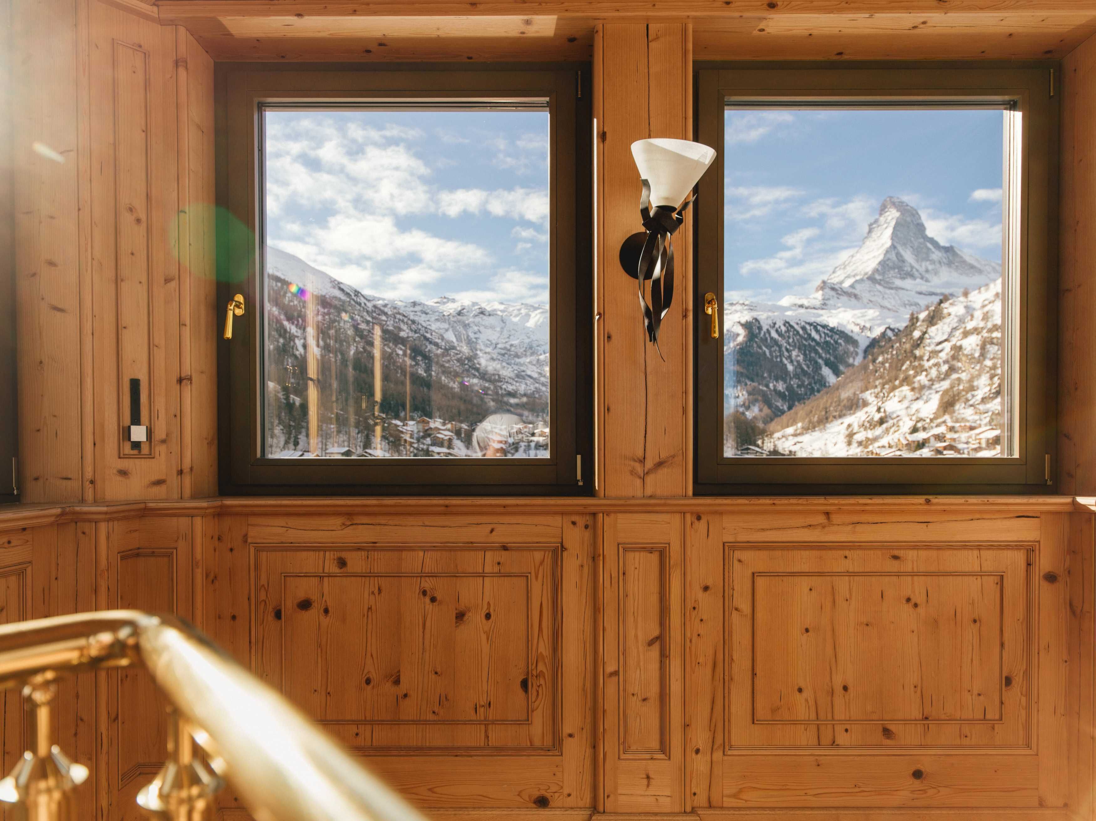 A wooden room with two large windows offering a view of a snowy mountain.