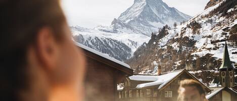 A mountain landscape with a prominent peak, a church with a green spire, and a building with a snow-covered roof.