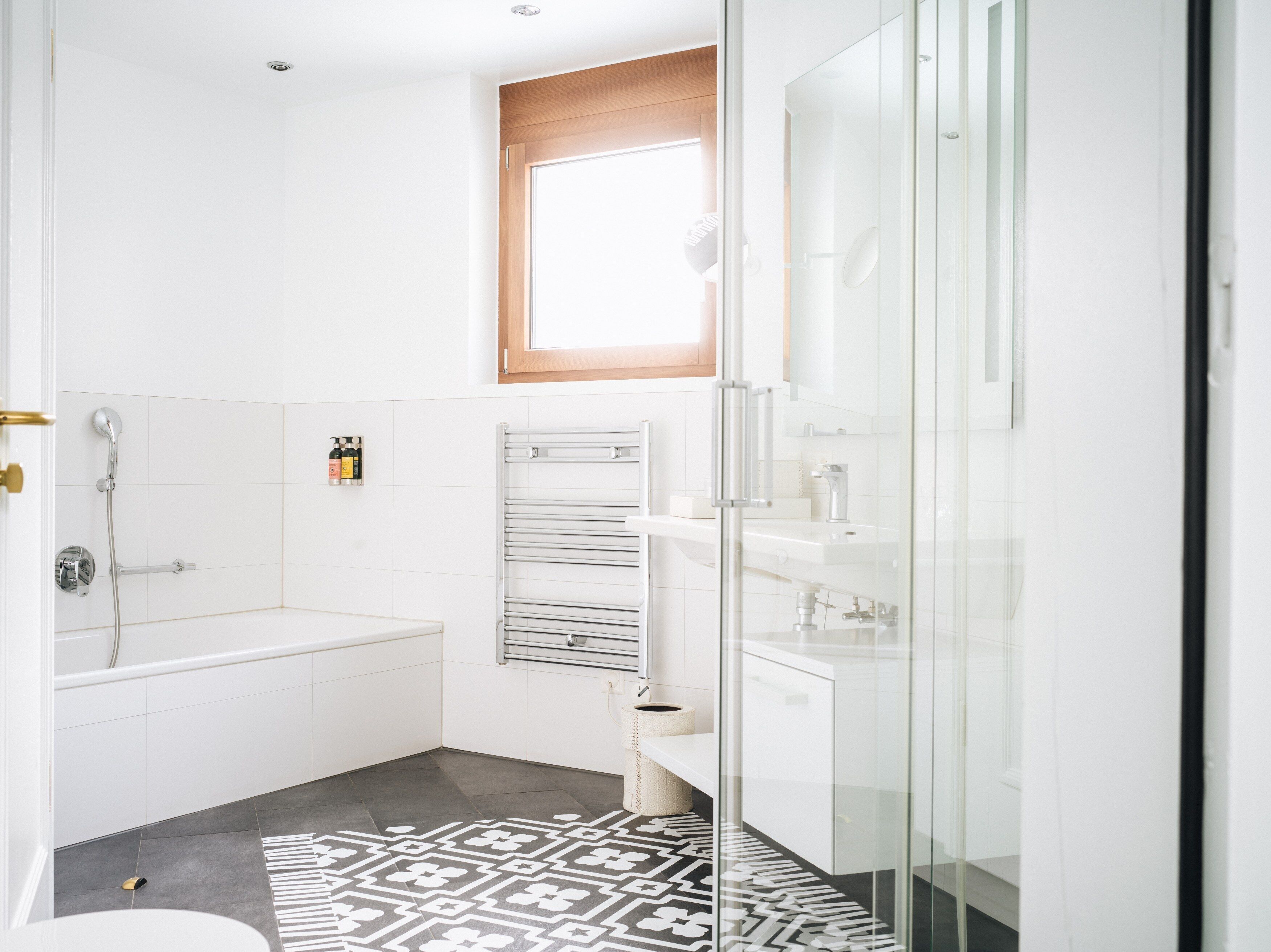A modern bathroom with a bathtub, a glass shower enclosure, and a patterned rug.