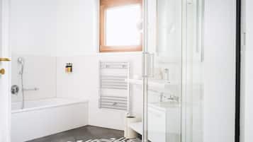 A modern bathroom with a bathtub, a glass shower enclosure, and a patterned rug.