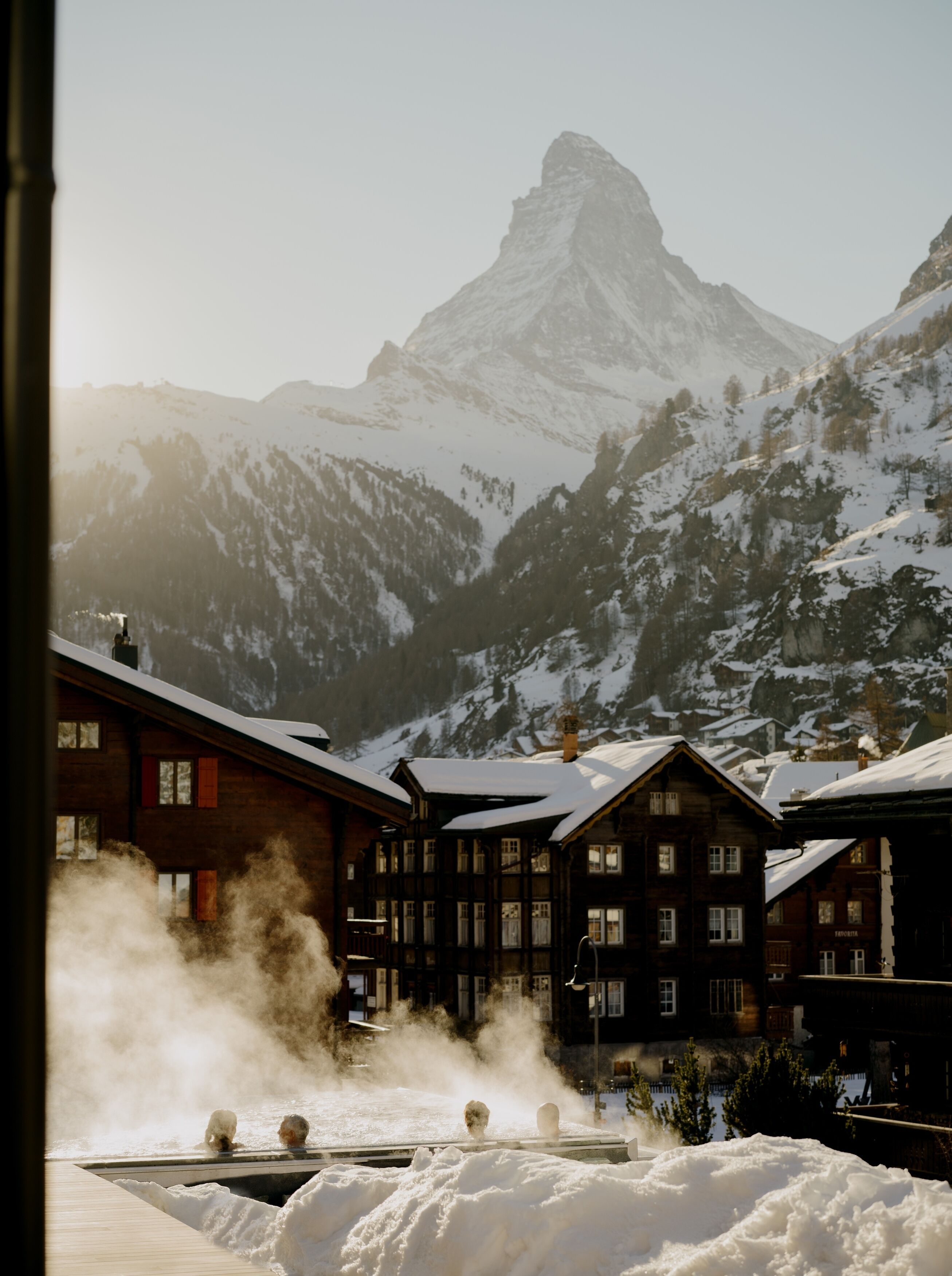 Un hotel con varias construcciones de madera, un patio cubierto de nieve y una montaña al fondo.
