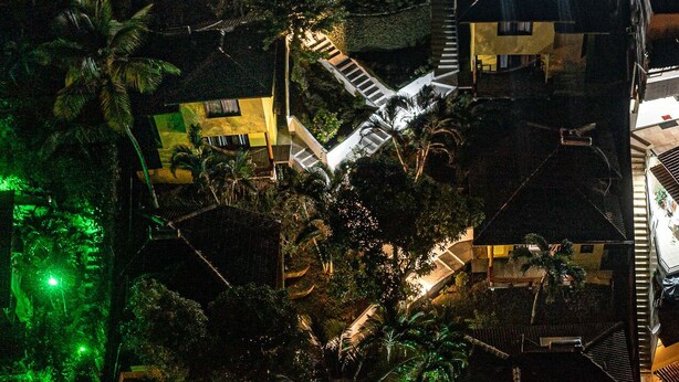 Vista aérea nocturna de una zona residencial con varias casas, una piscina y una escalera que lleva a una azotea.