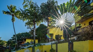 Una piscina con un edificio amarillo, palmeras y una hamaca.