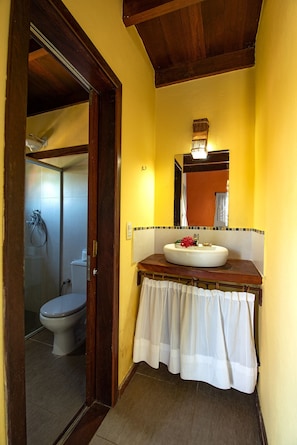 A bathroom with a wooden door, a white sink with a mirror above it, and a shower visible through the door.