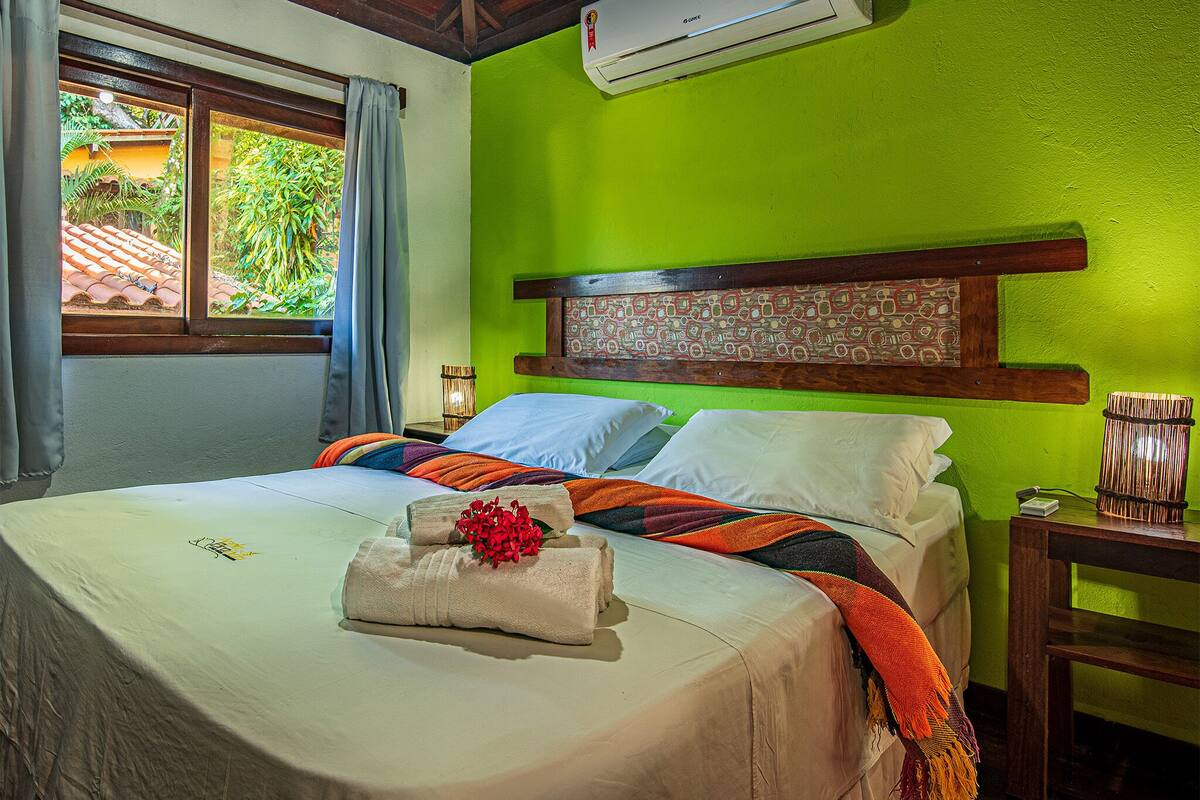 A hotel room with a bed, green walls, a wooden headboard, and an air conditioning unit.