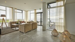 A spacious living area with a sofa set, a coffee table, and a lamp. Large windows offer a view of the sea. - Höfn - Berjaya Iceland Hotels (Höfn)