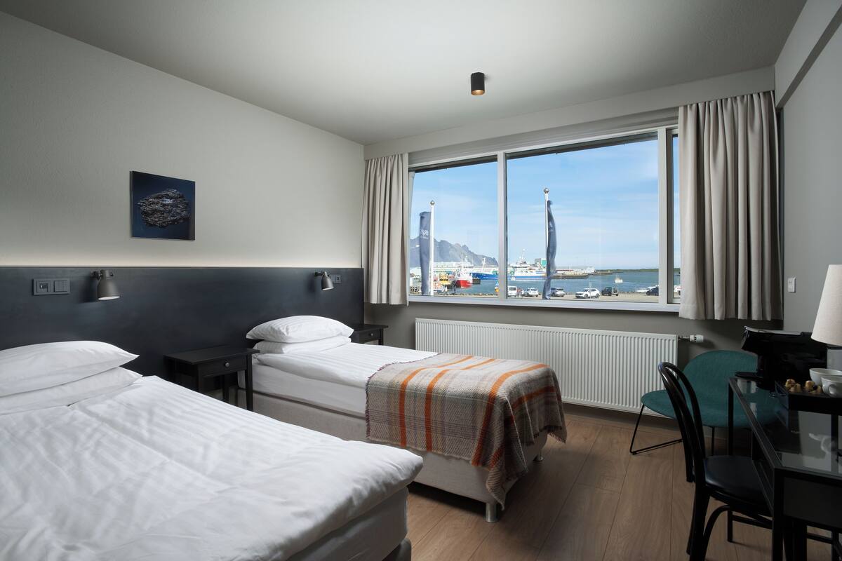 Une chambre d’hôtel avec deux lits, un bureau et vue sur le port.
