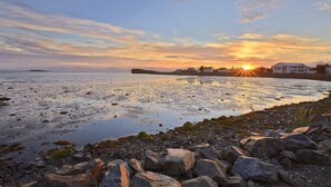A coastal landscape with a sunset, rocky shoreline, and a building in the background. - Höfn - Berjaya Iceland Hotels (Höfn)