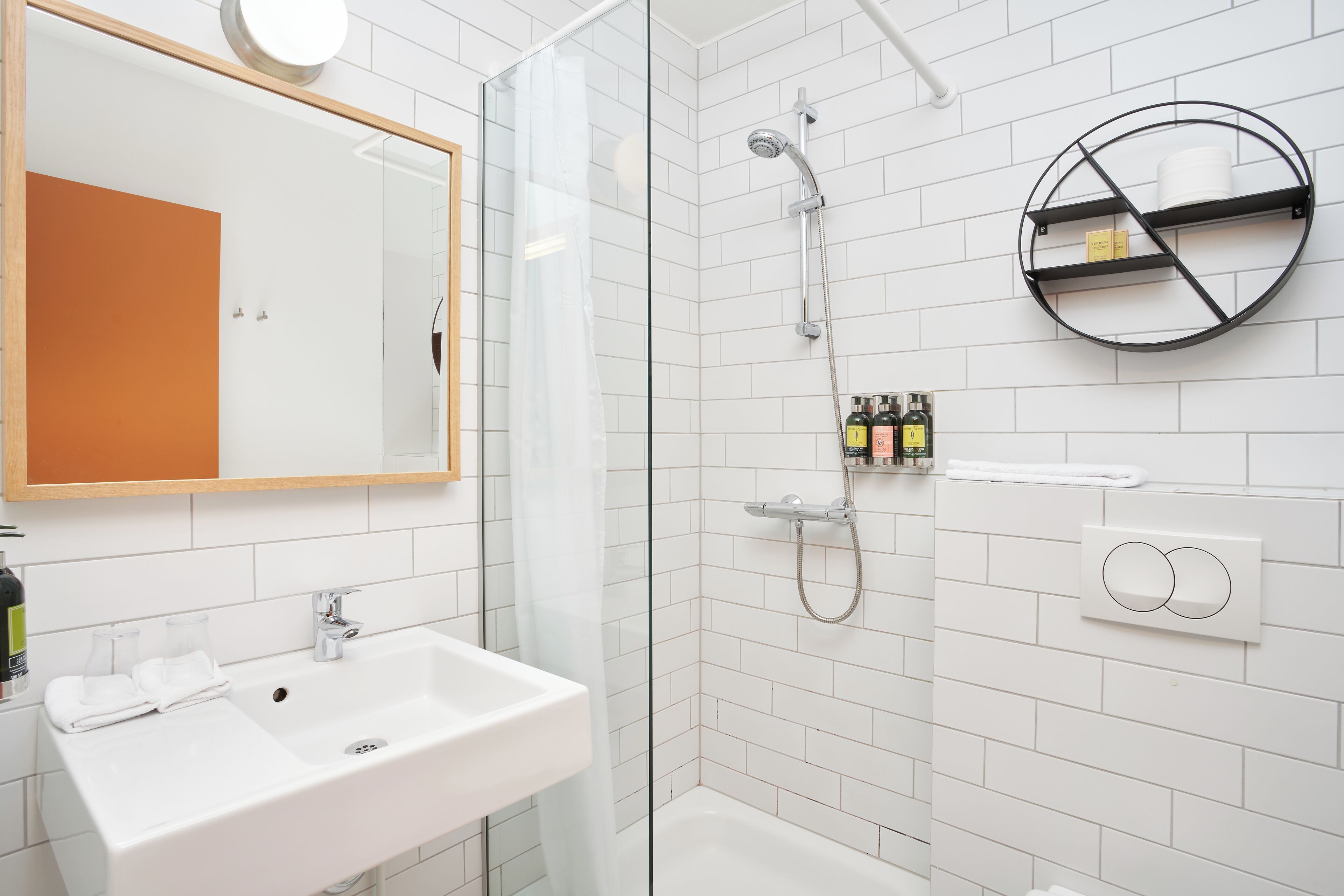A modern bathroom with a glass shower enclosure, a white sink, and a round shelf with toiletries.