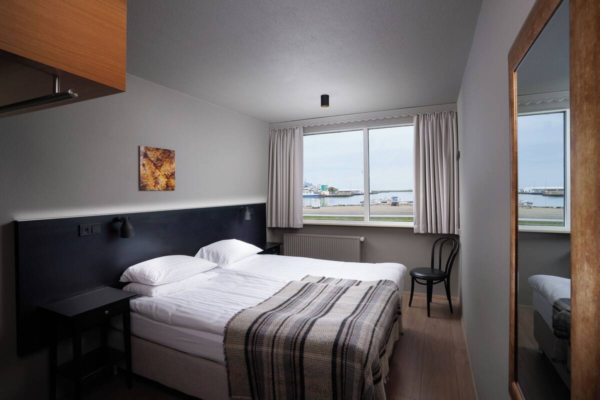 Une chambre d’hôtel moderne, dotée d’un grand lit, d’un bureau, d’une chaise et offrant une vue sur la mer par la fenêtre.