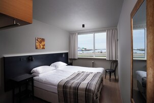 Una habitación de hotel moderna con una cama grande, un escritorio, una silla y vista al mar por la ventana.