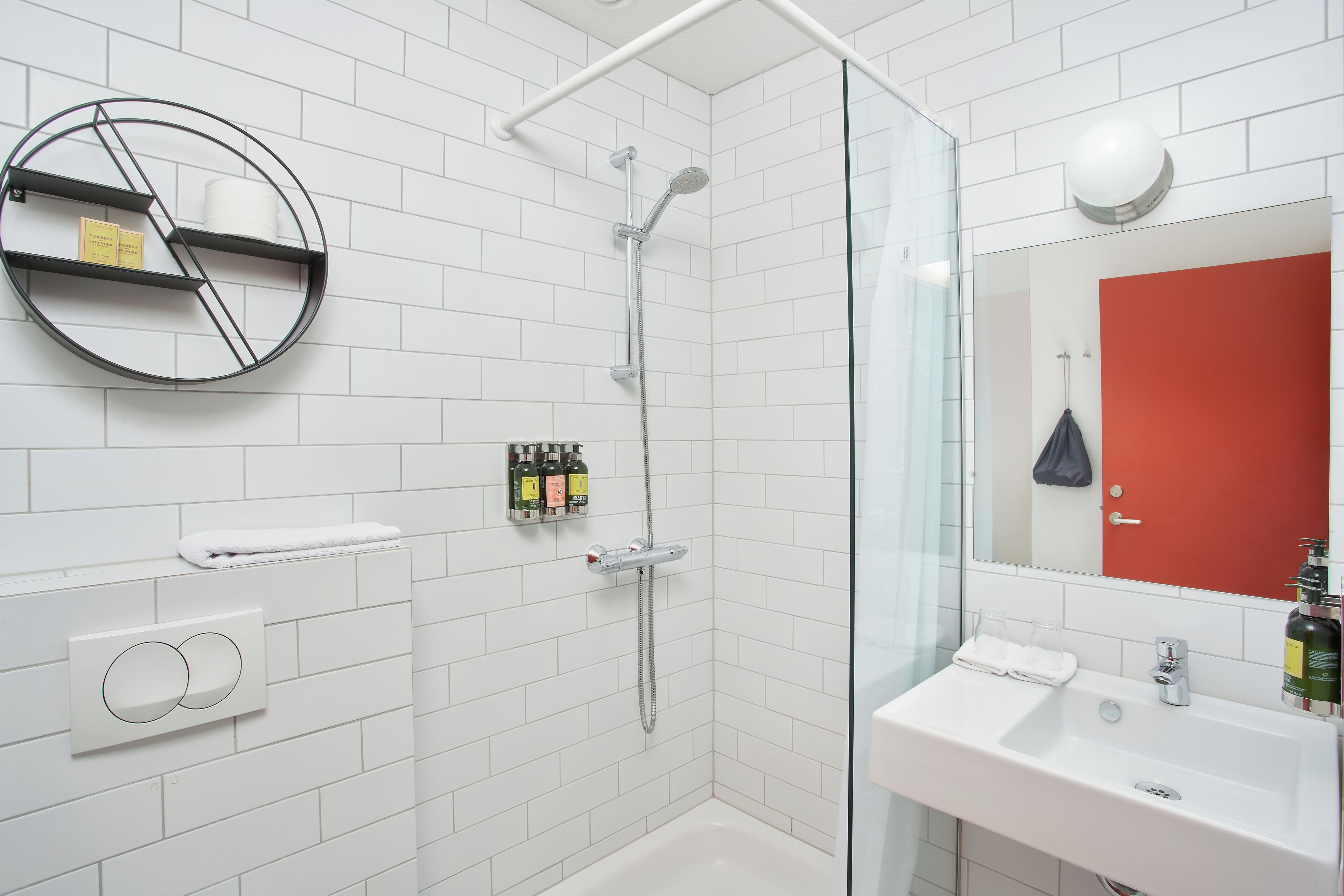 Un baño moderno con cabina de ducha de vidrio, un lavabo blanco y una repisa redonda con artículos de aseo.