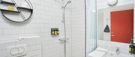 Un baño moderno con cabina de ducha de vidrio, un lavabo blanco y una repisa redonda con artículos de aseo.