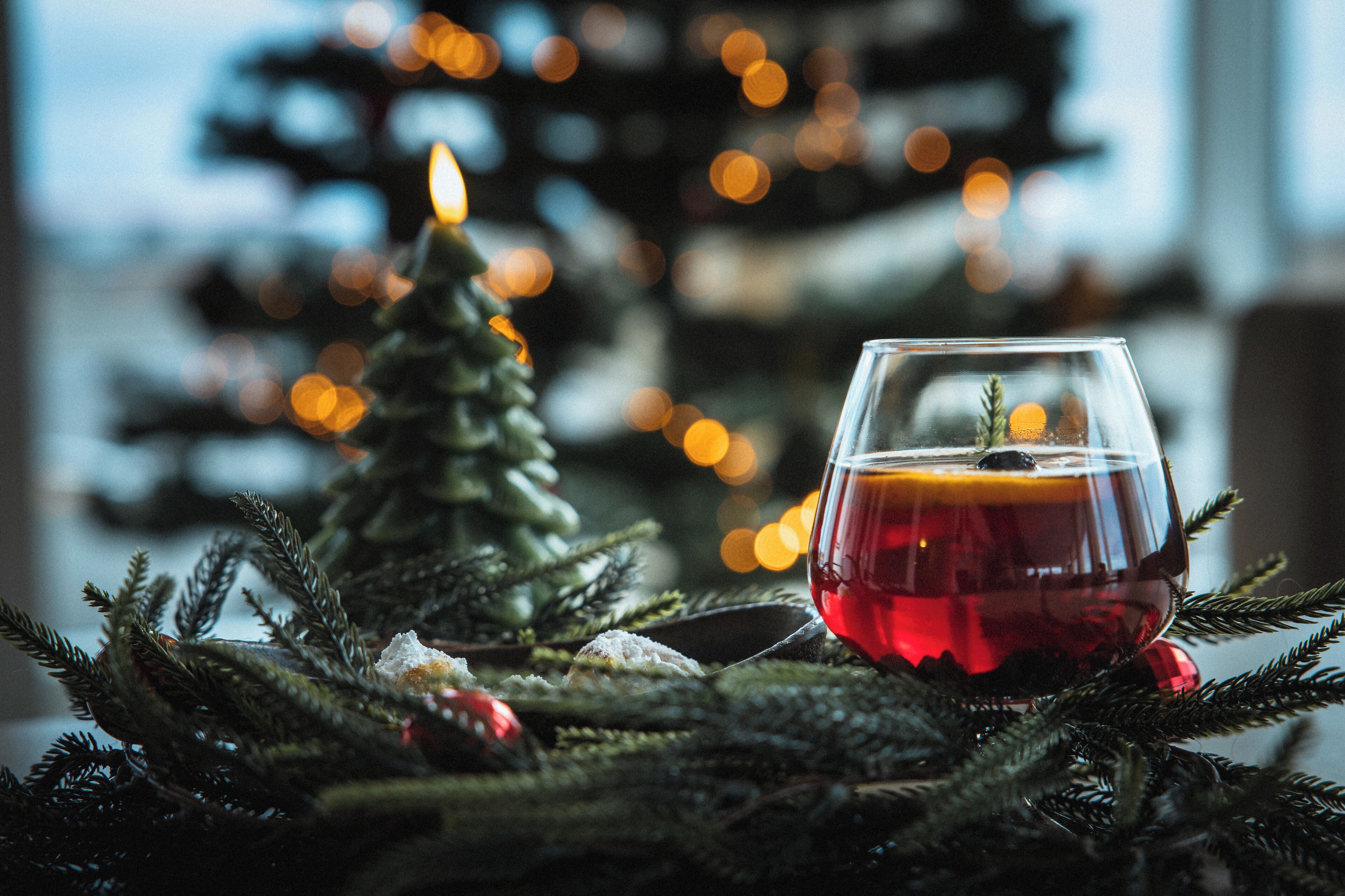 Un verre d’une boisson rouge posé sur un sapin de Noël, avec une bougie allumée.
