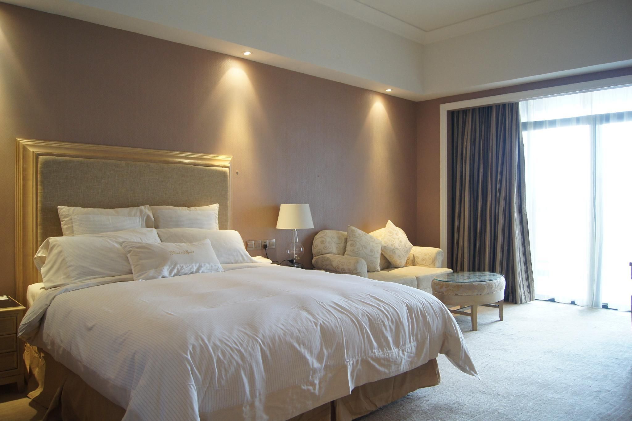 A hotel room with a large bed, a bedside table, a lamp, a chair, and a small round table.