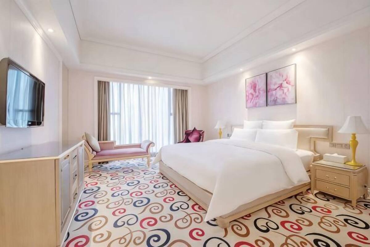 A hotel room with a large bed, a desk, a chair, a TV, and a window with curtains.