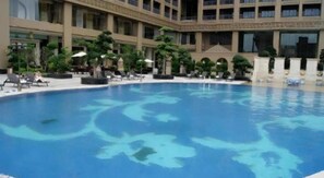 A swimming pool with lounge chairs and umbrellas, surrounded by a building with multiple floors and balconies. - Babylon Hotel (Dongguan)