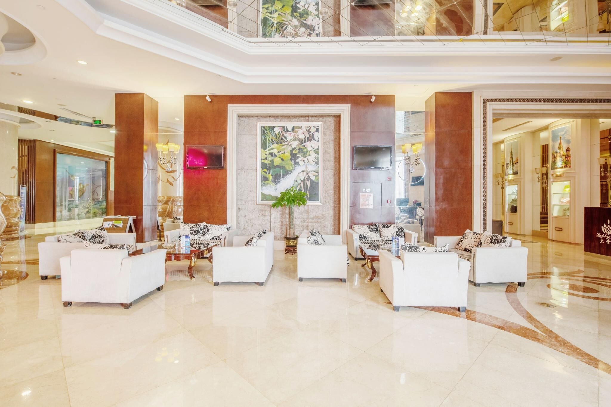 A spacious lobby with white sofas arranged in a semi-circle, a large mural, and a polished marble floor.