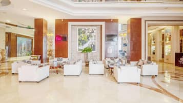 A spacious lobby with white sofas arranged in a semi-circle, a large mural, and a polished marble floor.
